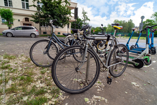 Several bicycles and electric scooters parked together. These modes of transportation are used for active travel on campuses and in cities. E-scooters, rental option in cities. To rent and park.