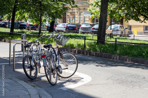 Several city bicycles locked to inverted-U style metal racks, Sheffield stands, on a paved sidewalk. The bicycles for urban commuting, featuring baskets, reflectors for increased visibility, utility. 