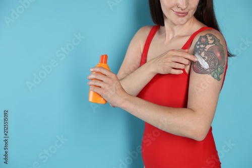 Konstfotografi Woman applying sunscreen onto her tattoo on light blue background, closeup