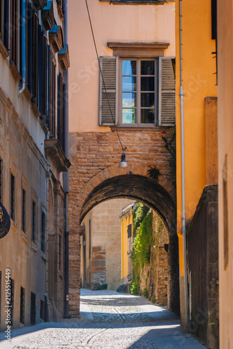 Narrow cobblestone street with archway and colorful buildings in Bergamo, Italy, showcasing historical architecture and vibrant facades