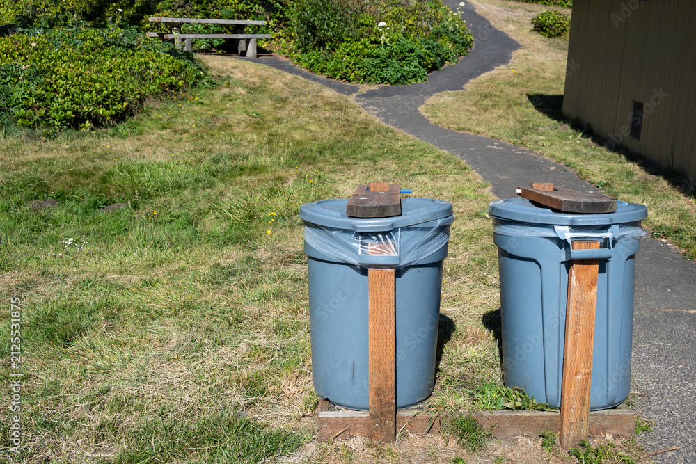 Obraz premium DIY, do it yourself, animal and wind proofed garbage cans, plastic trash bins reinforced with wood boards outdoors in a public park 