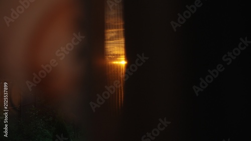 Fotografía Sunset light creating a vibrant orange glow and long reflections, glimpsing thro
