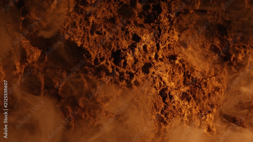 Naklejka premium Intense smoke rises from porous volcanic rocks illuminated by glowing orange light in a barren desolate landscape