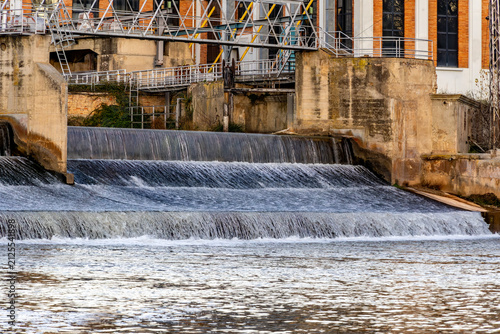 Konstfotografi Water flowing over concrete dam spillway near industrial building