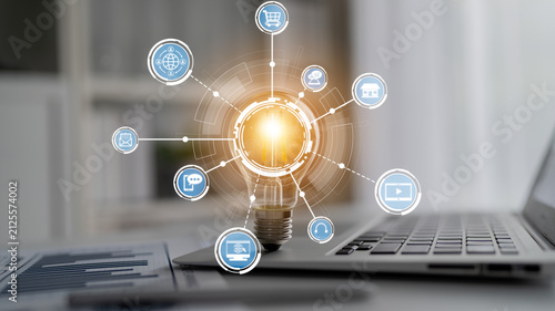 Fotografie This image features a light bulb representing creativity and innovation, surrounded by digital icons illustrating technology and online shopping in a modern workspace