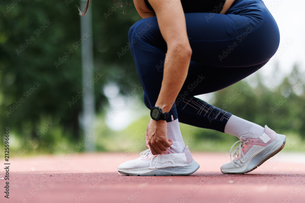Obraz premium Woman Tying Shoe Laces During Outdoor Workout Session on a Track