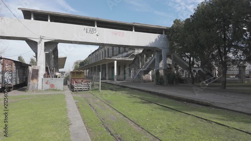 Zoom-in shot showing the concrete footbridge, platforms, and abandoned tracks at historic La Plata El Provincial station, Argentina. D-Log M, 10-bit color, flat log profile.