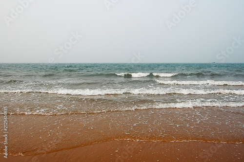 фотографія Calm sea waves gently rolling onto a sandy beach under a hazy sky