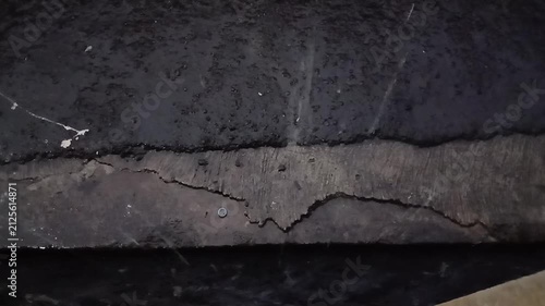 Close up shot of a deep crack and damage on a dark weathered asphalt or concrete ground surface