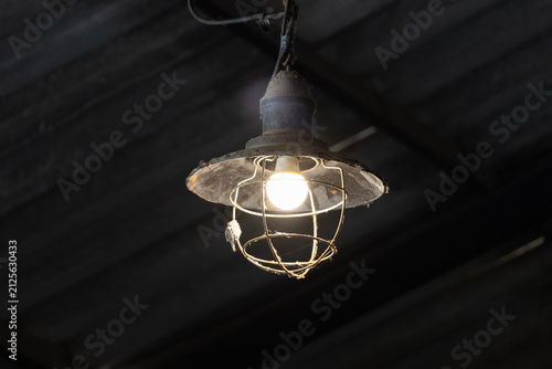 Obraz na plátně Old-fashioned cage lamp illuminates dim warehouse space