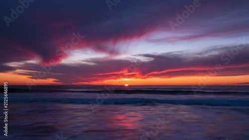 Vibrant ocean sunset with dramatic orange and red sky, sun rays reflecting on the water, and peaceful waves rolling onto the beach at dusk, showcasing natural beauty.