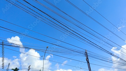 Bild auf Leinwand Overhead Power Lines Against Bright Blue Sky with White Clouds