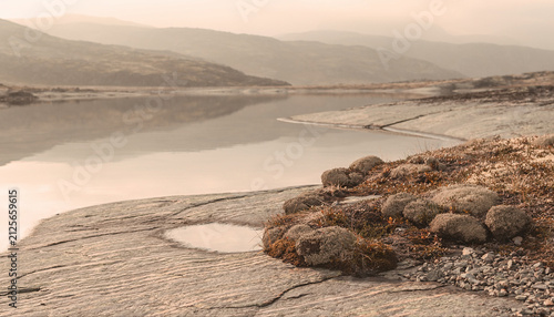Serene Rocky Shoreline with Calm Water and Misty Mountains in the Distance, Ideal for Nature and Tranquility Themes