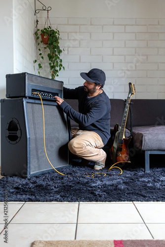 Hispanic man crouching down to tune sound settings on guitar amp in living room