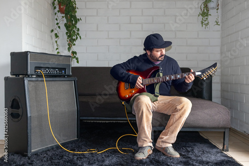 Fotografie Hispanic man practicing guitar chords at home with guitar amp stack