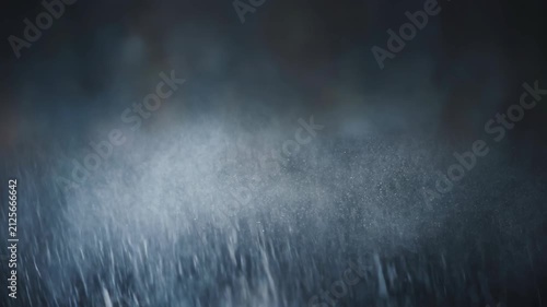 Rain falling on dark surface creating misty atmosphere for dramatic effect