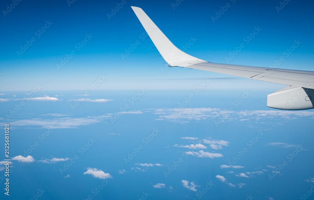 Fototapeta premium Commercial airplane wing seen from passenger window while flying above clouds under clear blue sky. Modern aviation, international flight, travel experience and tourism concept. Global tourism.