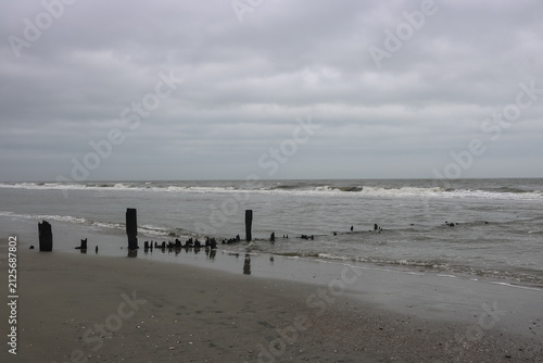 Bild auf Leinwand weathered pilings disappear into the Atlantic Ocean, remnants of an old pier on a gray cloudy day
