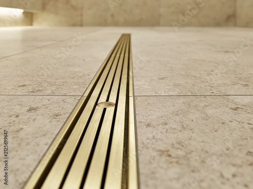 Brushed brass linear shower channel drain in modern spa bathroom with stone tile