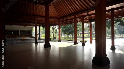 Interior of a traditional Javanese wooden building featuring sturdy support pillars and a lush courtyard atmosphere.