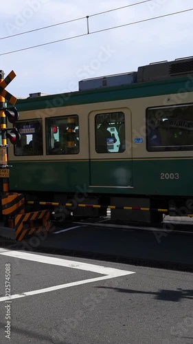 Enoden train passing a railway crossing near the sea in Kamakura, Japan, with ocean view, road markings and coastal travel atmosphere. Travel, transportation and sightseeing background.