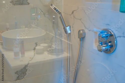 Modern walk in shower with glass partition, handheld showerhead and marble wall tiles. Contemporary bathroom design, hygiene and comfortable daily living.