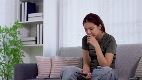 Frustrated young Asian woman feeling anxious while using smartphone on couch in modern living room with copy space