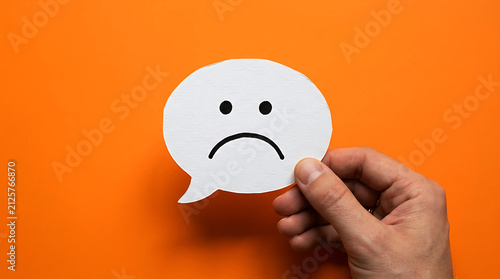 Fototapeta kuchenna Hand holding a white speech bubble with a sad face icon on an orange background