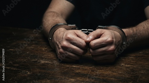 Handcuffed Hands Resting on Dark Wooden Table