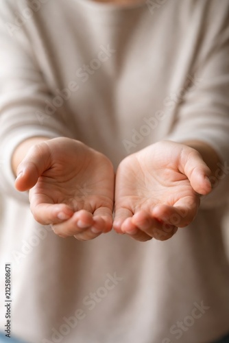 Open hands of a person with light skin, palms facing up, positioned in front of a neutral background, suggesting offering or receiving something