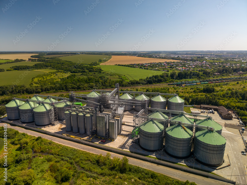 Obraz premium Elevated panoramic perspective of modern agricultural grain storage facility with green roof metal silos built in rural landscape.