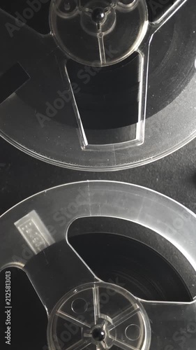 Vertical close up of a reel to reel tape recorder with two transparent spools of magnetic tape rotating. Retro analog audio equipment for vintage sound and archive footage