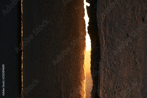 Narrow crack in rough concrete wall reveals bright golden sunset glow