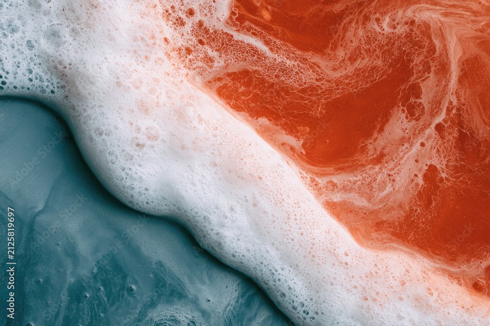 Fototapeta premium Abstract close-up of orange and blue liquids swirling with white foam