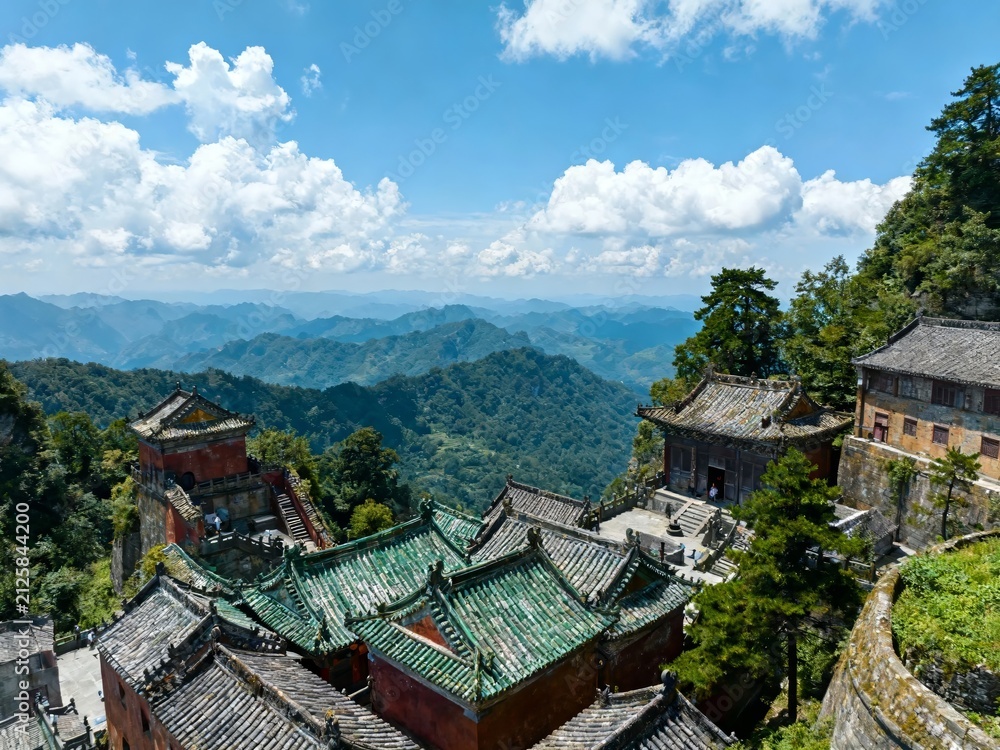 Fototapeta premium Traditional temple complex with green tiled roofs nestled among mountains under a bright blue sky