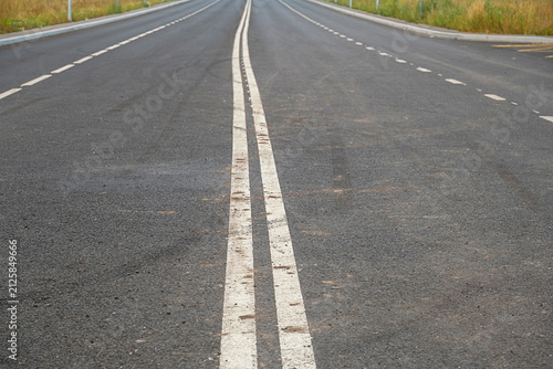 Asphalt road with double solid white line markings. Perspective view of highway lane separation.