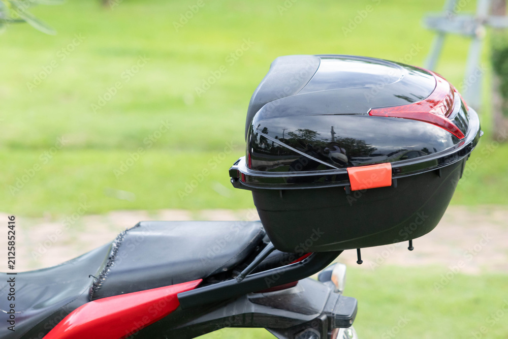 Fototapeta premium Motorcycle with black storage box and red accents on grassy roadside