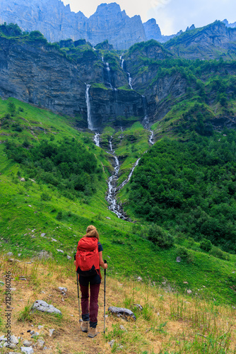 Принти на полотні Rear view of female hiker with red backpack walking towards dramatic mountain wa