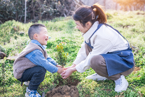 Canvas Print An adult and a young child crouch together outdoors, holding a small sapling to plant, showing a warm cooperative activity