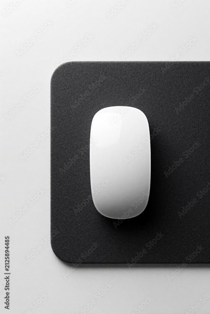 Obraz premium White wireless computer mouse sits on black textured pad. Minimalist top view shows sleek hardware for modern office desk. Simple digital tool provides smooth control for workspace productivity. High