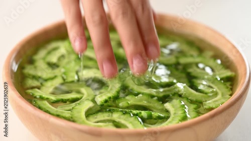Woman hands soaking a sliced bitter gourd with salt and water in a wooden bowl to reduce bitterness