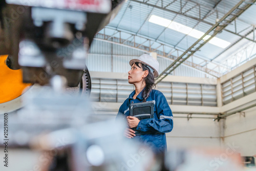 Female engineer with tablet inspecting large press machine on factory production floor