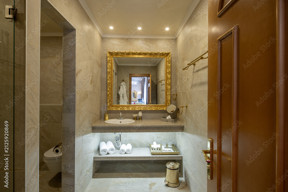 Obraz premium Elegant hotel bathroom interior with golden mirror and white towels