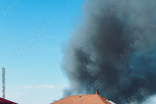 Obraz na płótnie Thick black smoke plumes rise into the sky from a fire behind residential roofto
