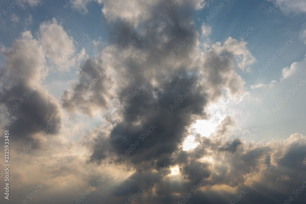 Obraz premium Dramatic sunbeams shining through dark clouds in blue sky during afternoon