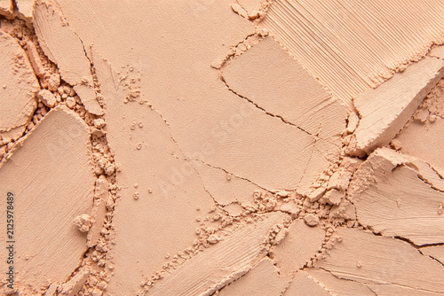Crushed beige pressed powder macro texture with cracks and cosmetic smears. Nude face foundation background for beauty editorial, skincare branding and product design.