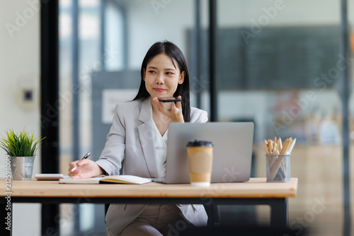 Canvastavla Asian businesswoman using voice assistant on smartphone and writing notes, multi