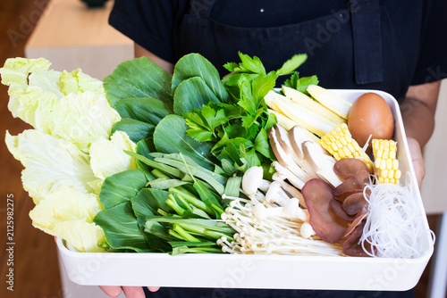 Waitress holding tray of fresh vegetables mushrooms corn egg and glass noodles for hotpot or shabu shabu.