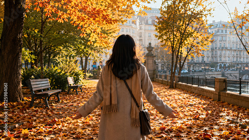 Expat autumn homesickness. Back view of an Asian adult standing on a path covered in fallen autumn leaves in a foreign city park, in the unfamiliar season