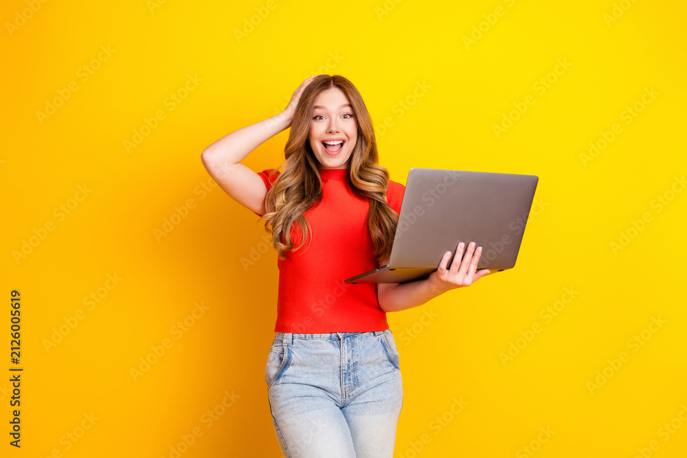 Fototapeta premium Surprised young woman holding laptop and smiling on yellow background, remote work and online learning technology concept